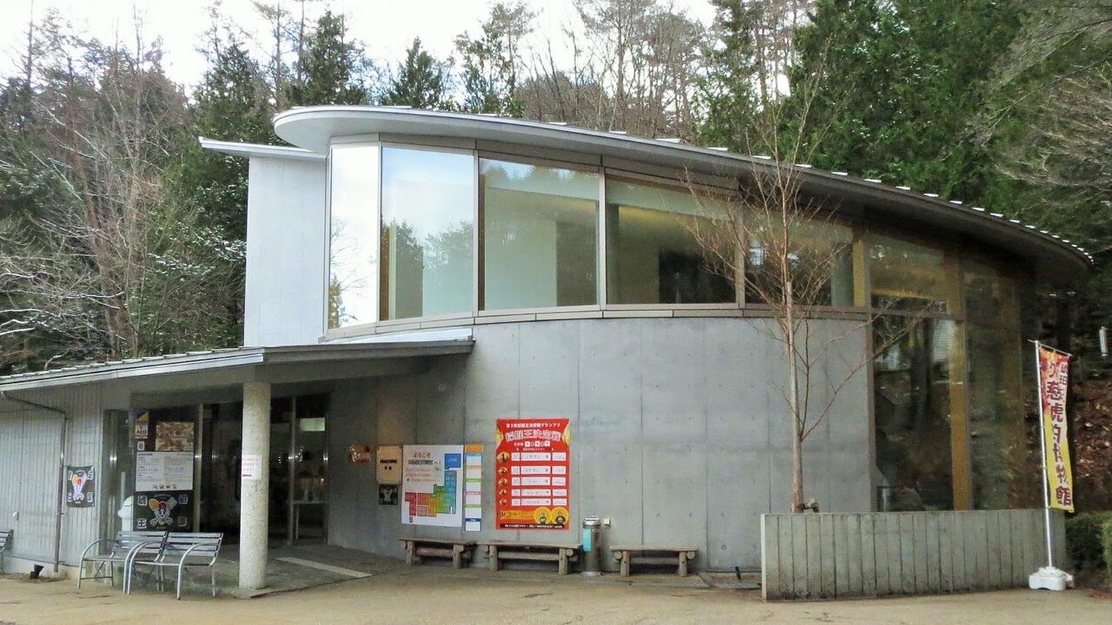 The Kuji Amber Museum building, a low concrete and glass hall with a curved metal roof, with a banner outside and forest behind