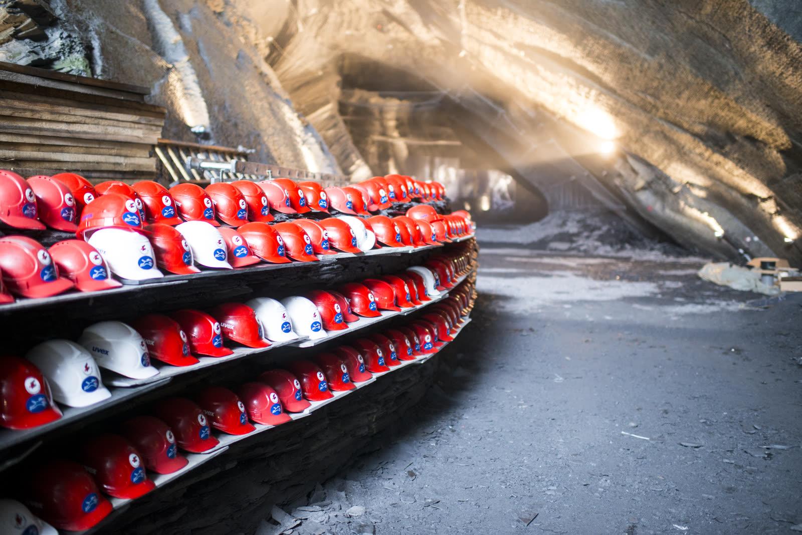 Rows of red and white visitor helmets on a shelf beside a lit slate gallery inside the Landesplattenberg mine