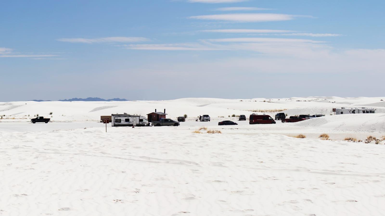 Bright white gypsum dunes with parked RVs and trucks at a roadside pull-out at White Sands National Park, New Mexico.