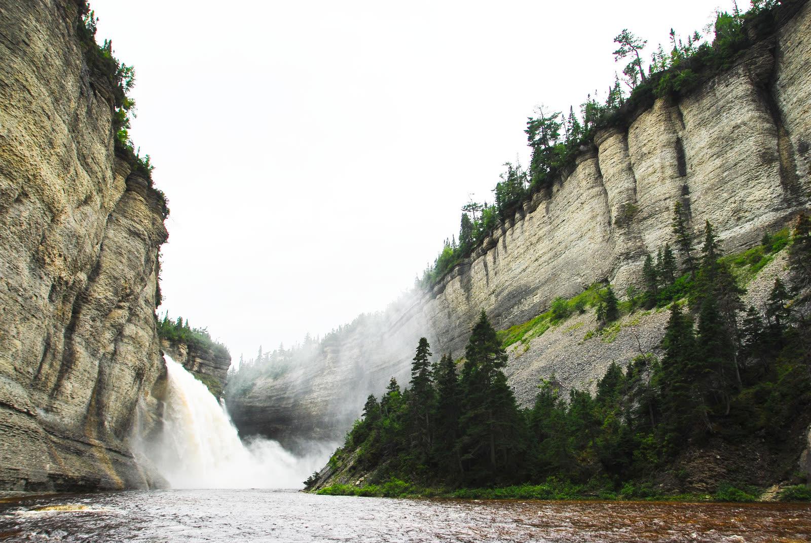 Sheer layered canyon wall beside Vauréal Falls with spruce trees on the slope below