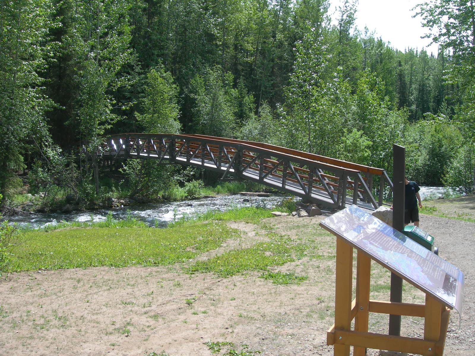 Wooden footbridge arching over Driftwood Creek at the start of the Driftwood Canyon interpretive trail, with a trail panel in the foreground