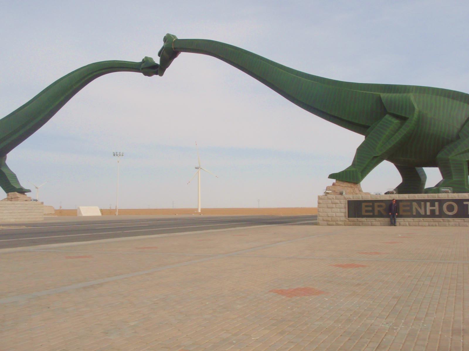 Two green sauropod sculptures arching over a road with their heads meeting above the carriageway, ERENHOT lettered on the plinth