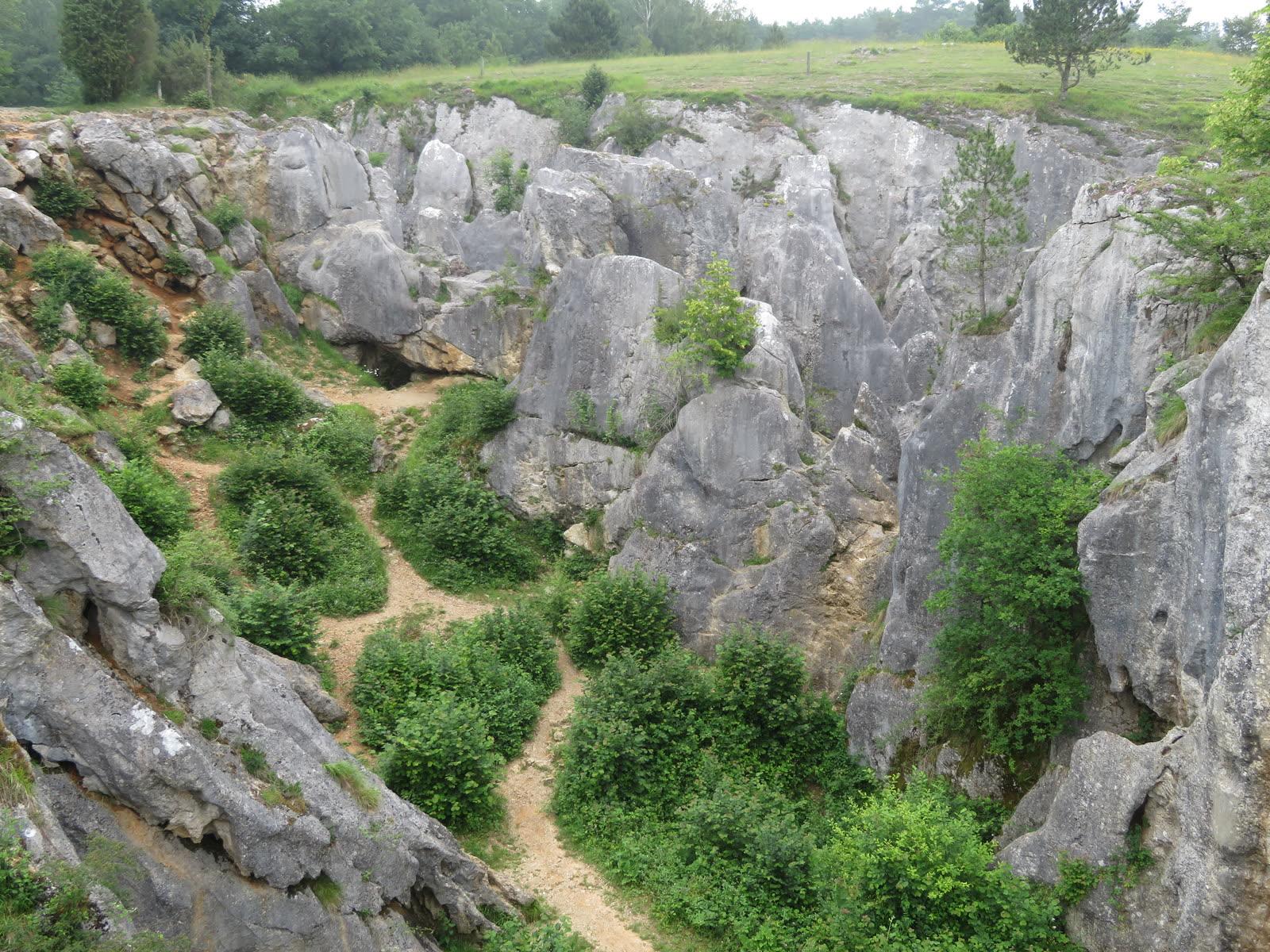 Grey limestone walls and a dirt path in the Fondry des Chiens sinkhole seen from the rim