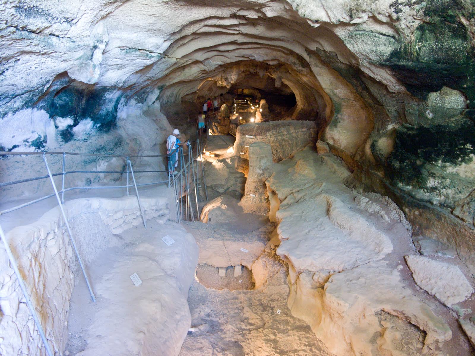 A pale scalloped limestone cave with a railed walkway and a visitor descending steps inside Għar Dalam