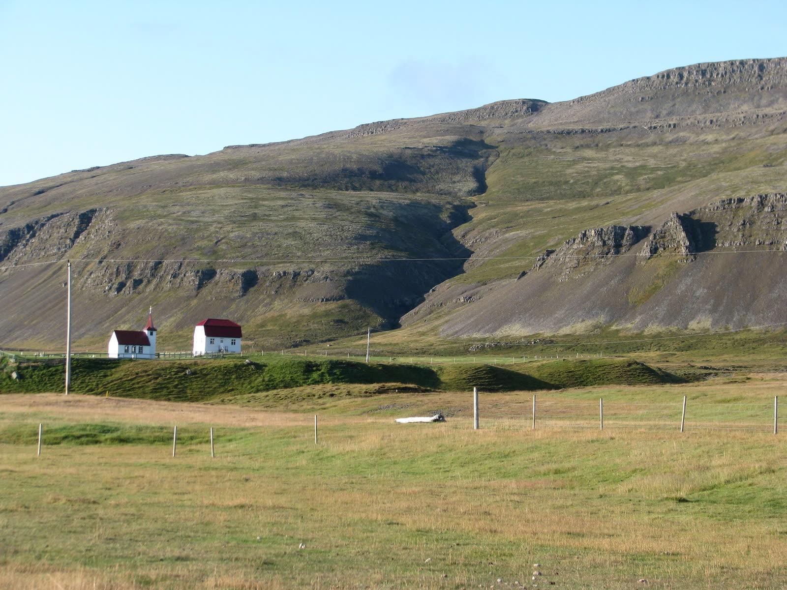 A small white church and red-roofed farm building below a steep terraced mountainside at Brjánslækur