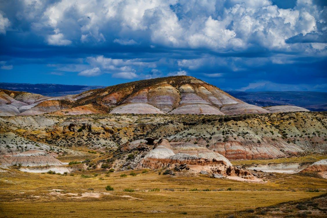 Striped pink, orange and grey hill rising above a grassy meadow under a dramatic cloudy sky near Fossil, Oregon.