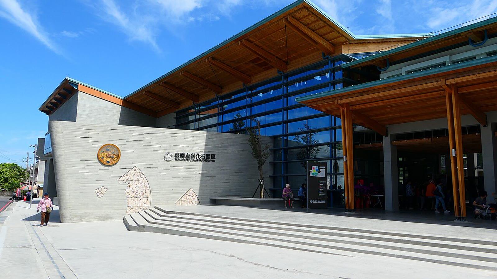 The entrance plaza of Tainan City Zuojhen Fossil Park, a concrete and timber building with a wide pitched canopy and the park name on the wall