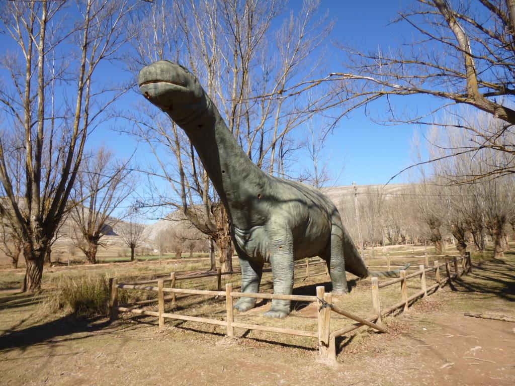 Life-size sauropod dinosaur sculpture behind a wooden fence in a wintry park along the Galve dinosaur trail, Teruel.