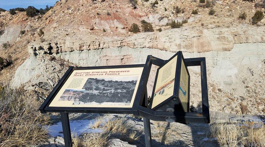 Interpretive sign about shifting streams and dinosaur fossils standing in front of layered cliffs at Garden Park.