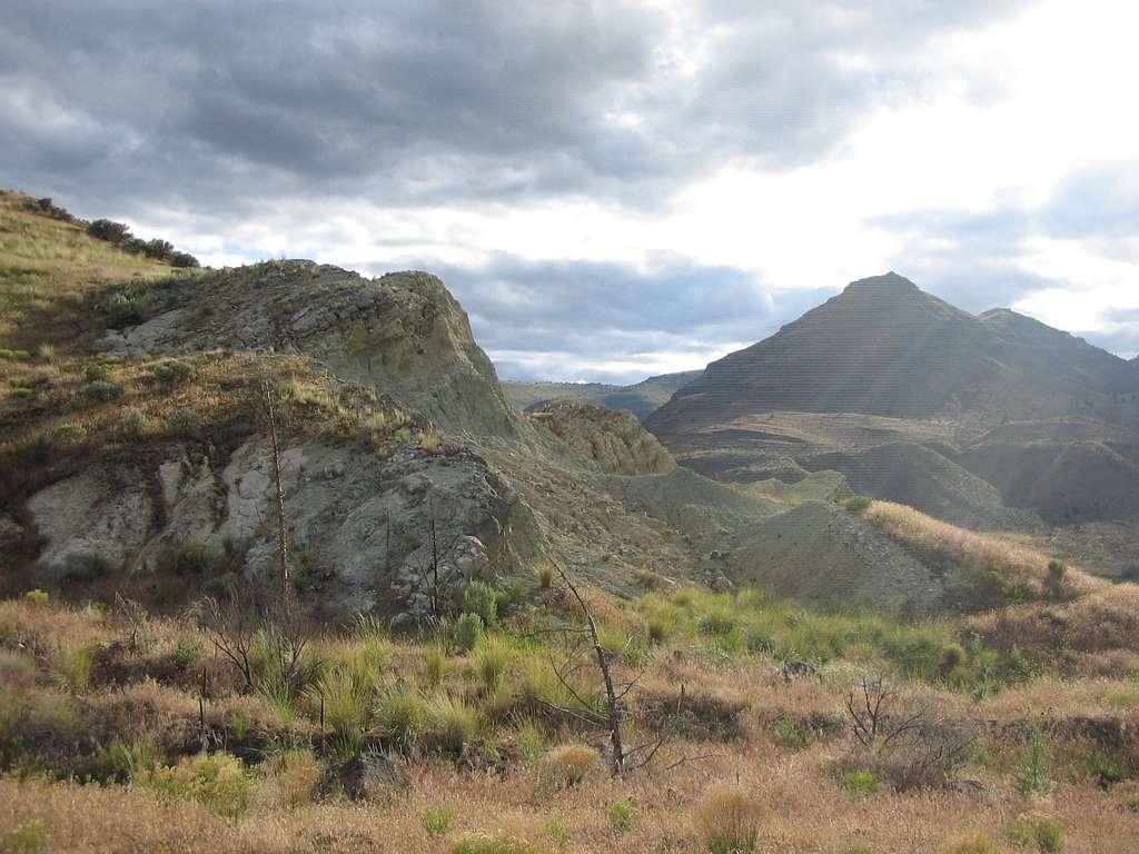 Rolling grassy hills with eroded greenish slopes and a pyramid-shaped peak at John Day Fossil Beds, Oregon.