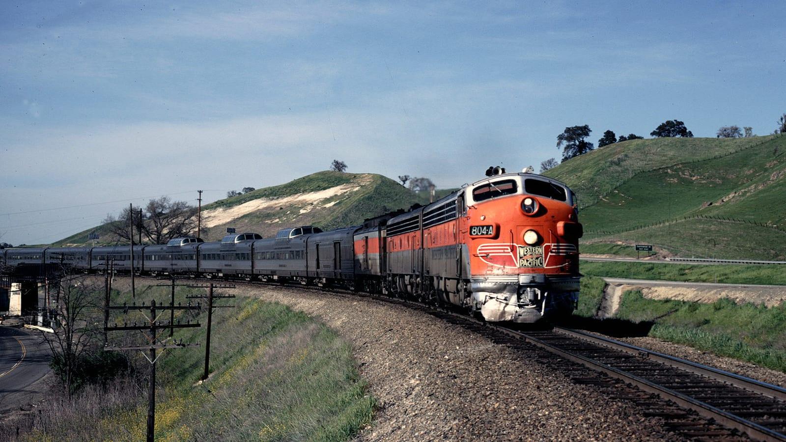 Vintage red Western Pacific passenger train curving through a railroad cut with oak-studded hills near Pleasanton.