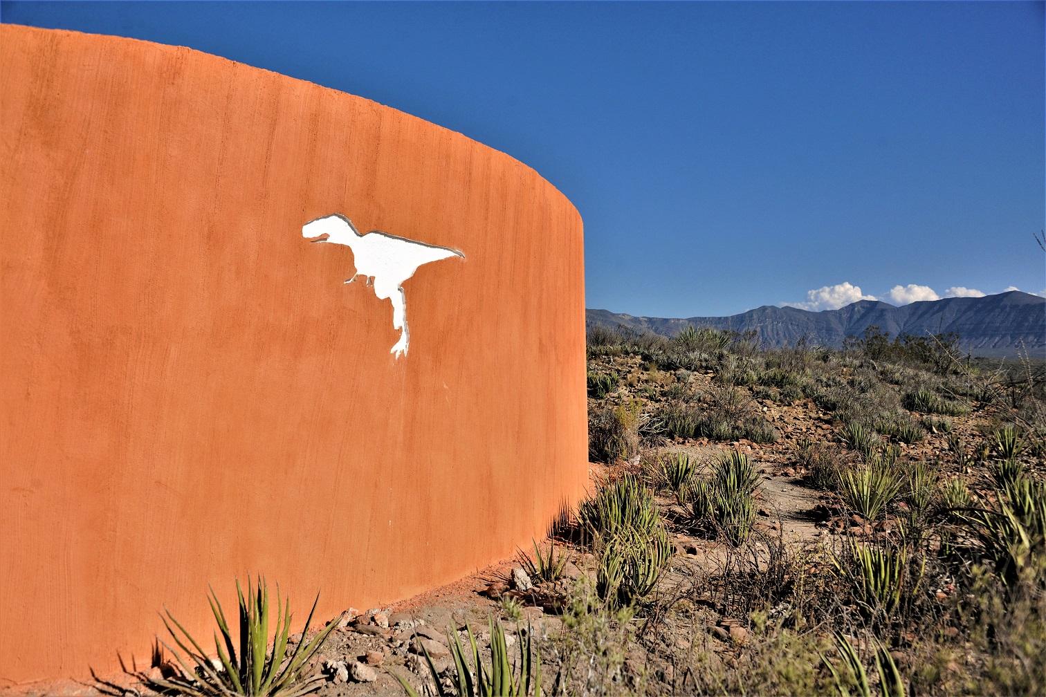 Curved orange wall with a cut-out dinosaur silhouette at the entrance to the Rincón Colorado area, Coahuila.