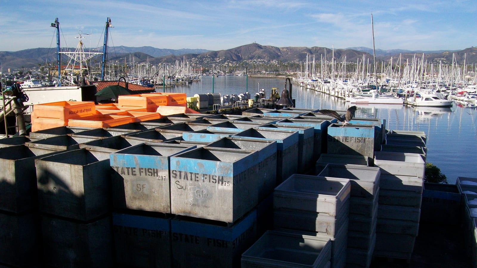 Stacked plastic seafood crates and moored sailboats in the Ventura Harbor marina near Surfer's Knoll, California.