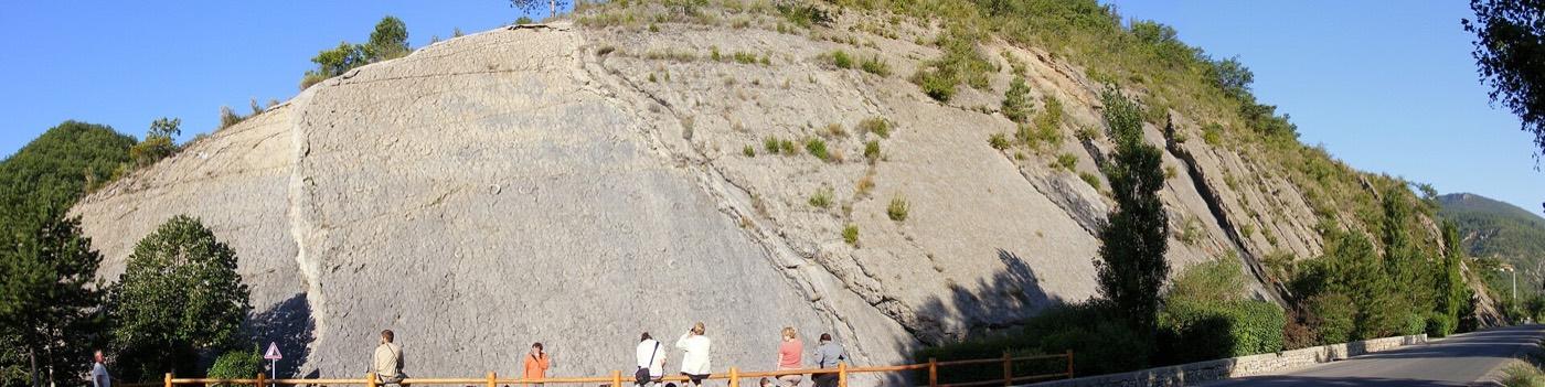 Wide view of the tilted ammonite slab near Digne-les-Bains with visitors on the path below