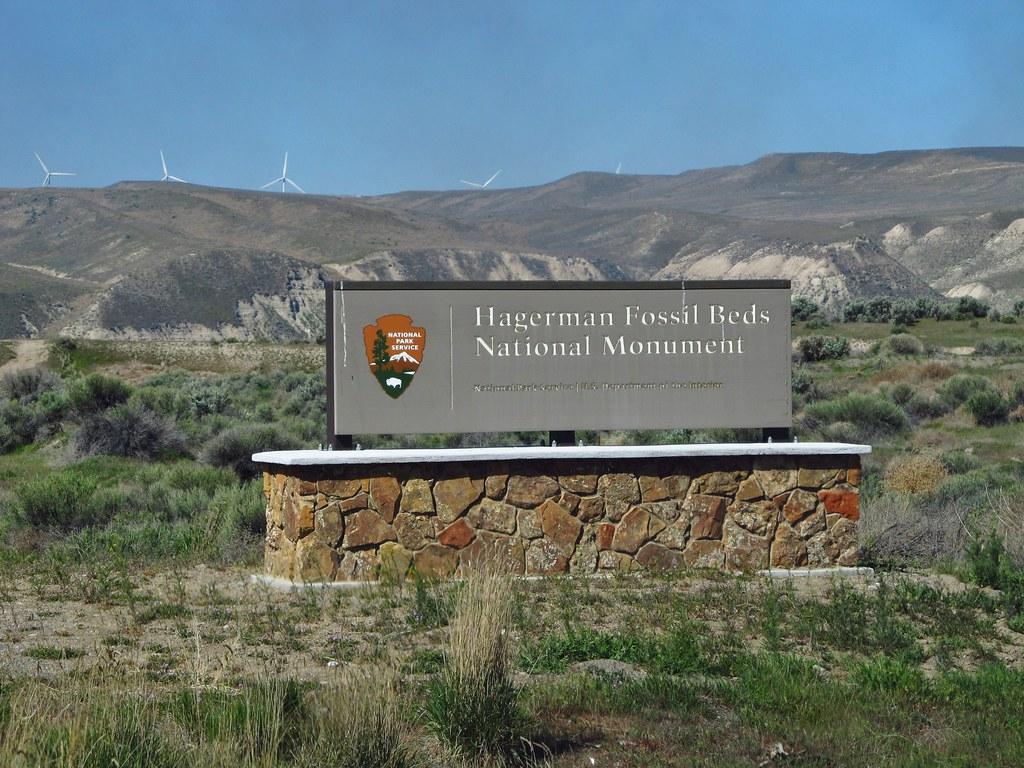 National Park Service entrance sign for Hagerman Fossil Beds National Monument with wind turbines on the ridge behind.