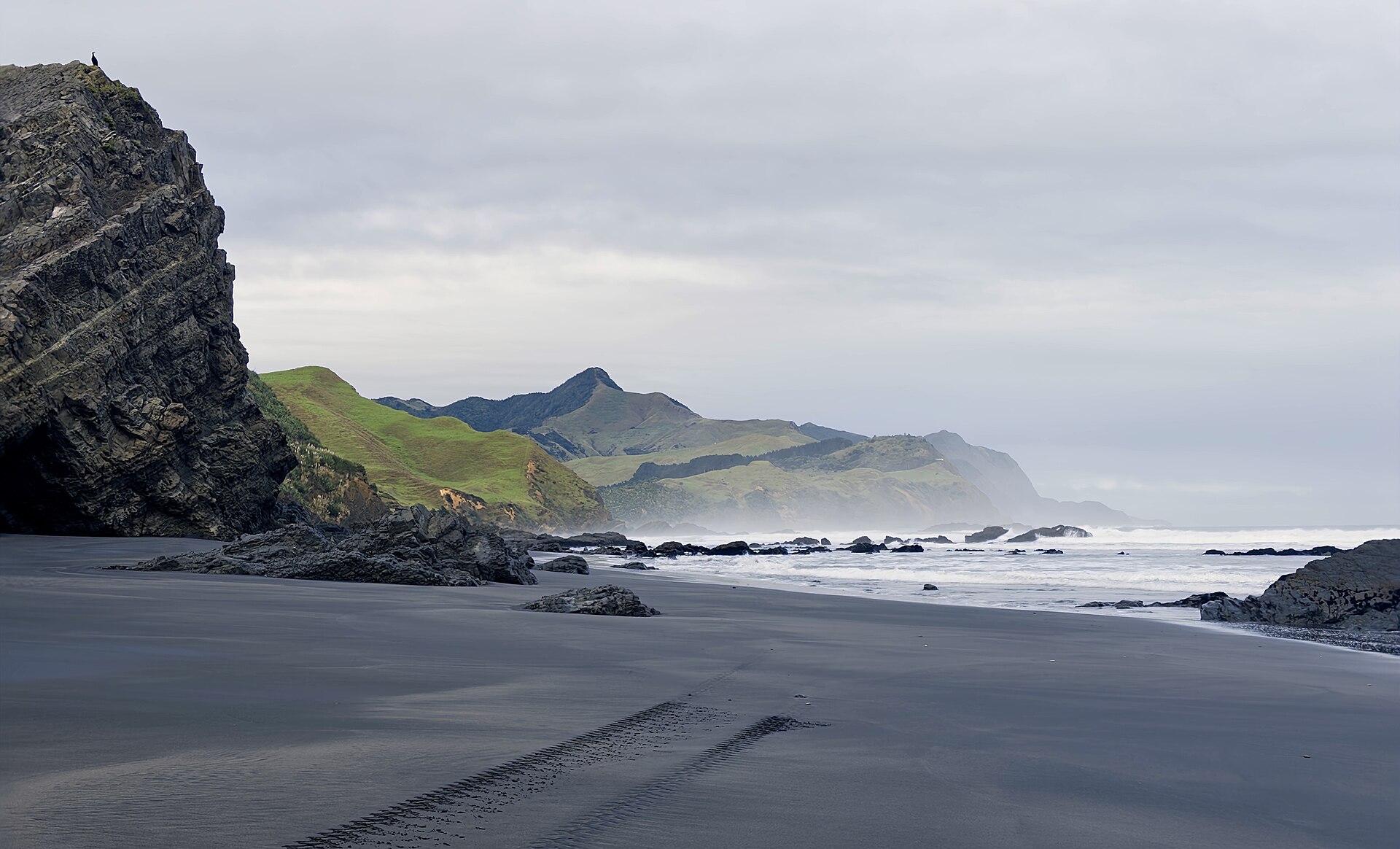 The dark sand of Marokopa Beach curving south beneath coastal cliffs