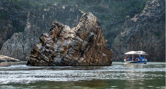 Tour boat passing tall striated cliffs along the river gorge at Lameta Geological Park, Madhya Pradesh, India.