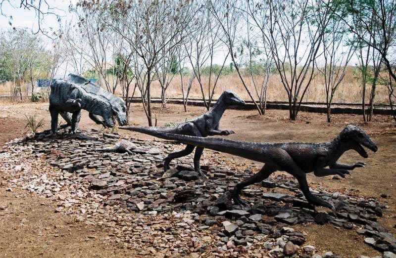 Several painted concrete dinosaur sculptures arranged on a gravel garden under bare scrub trees at Vale dos Dinossauros.