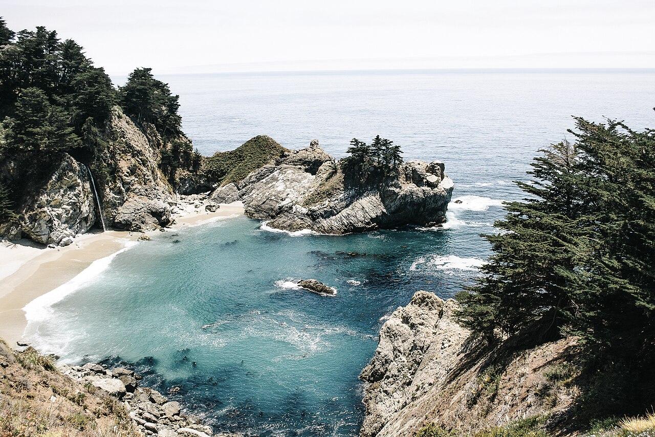 The Pacific breaking into a turquoise cove below steep wooded cliffs at Big Sur, California