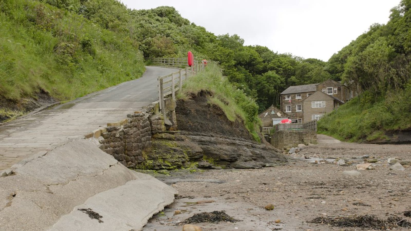 Concrete slipway dropping past a stone cottage to the sand and rock beach at Boggle Hole on the Yorkshire coast.