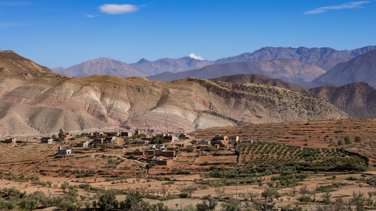 Village of low buildings nestled below striped sediment slopes near the Filon 12 mine area, Mibladen, Morocco.