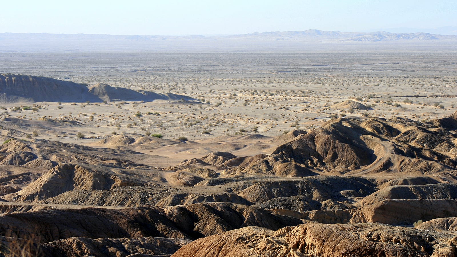 Vast eroded badlands of low arid mounds with distant mountains under hazy sky near Ocotillo, California.