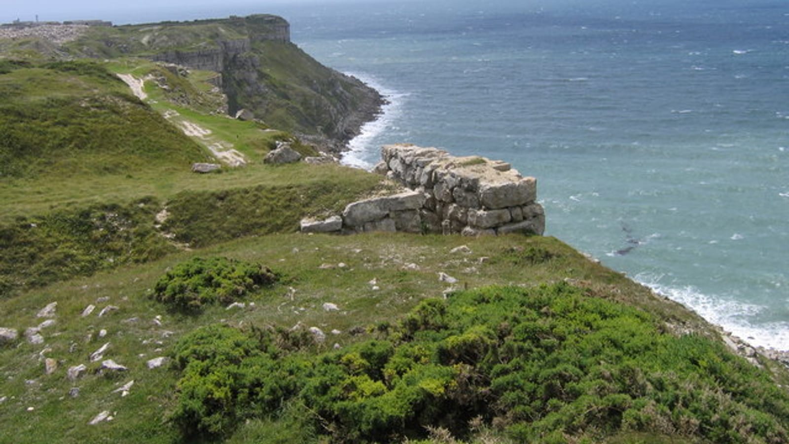 Grassy clifftop with rocky outcrops dropping to the rugged turquoise coastline of the Isle of Portland, Dorset.