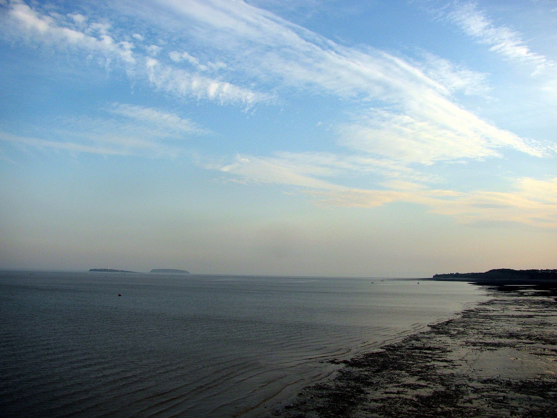 Hazy view across the Severn Estuary with low islands silhouetted and exposed mudflats at Penarth Beach, S. Wales.